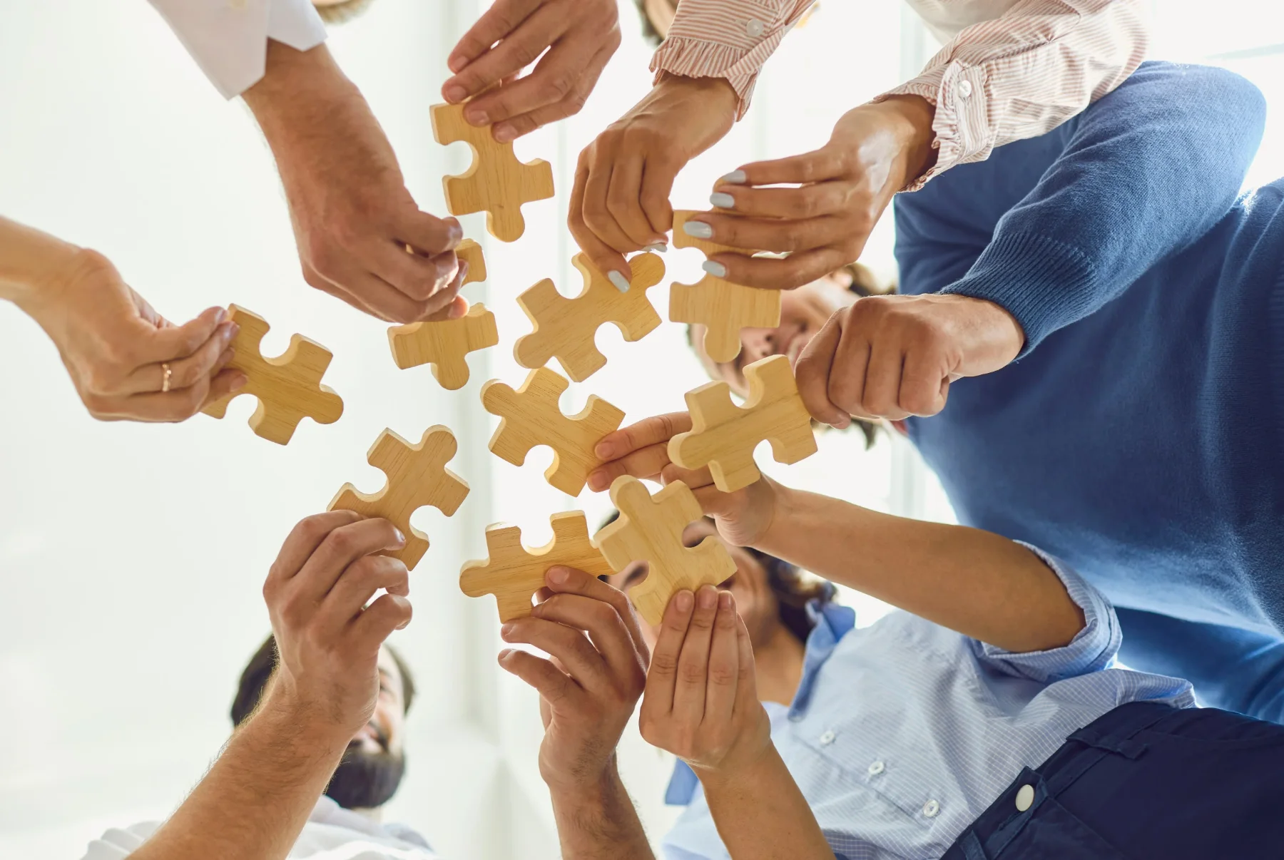 Several hands fitting wooden puzzle pieces together, representing building alternative responses to smoking triggers